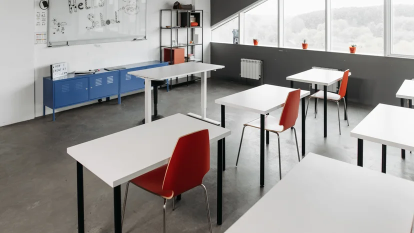 An empty classroom with white desks and red chairs, illustrating the school sector