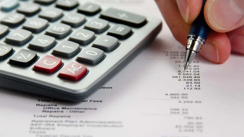 A hand using a pen to check financial figures beside a calculator