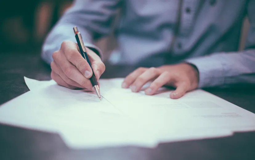 A person in a shirt signing a printed document with a pen.