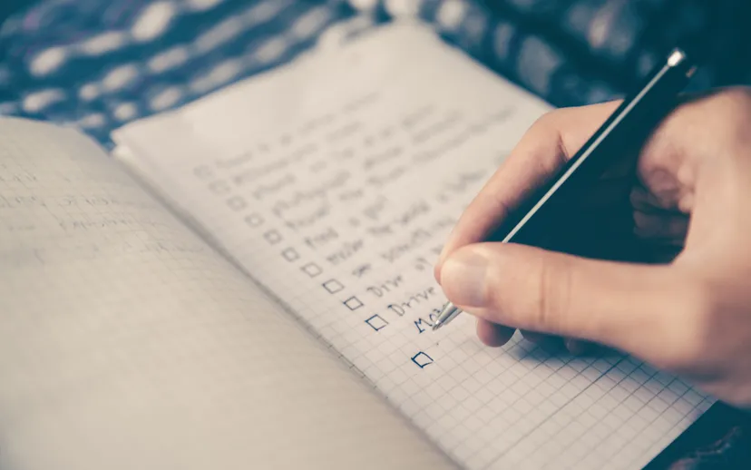 A hand writing in a notebook with a ticked checklist on squared paper.