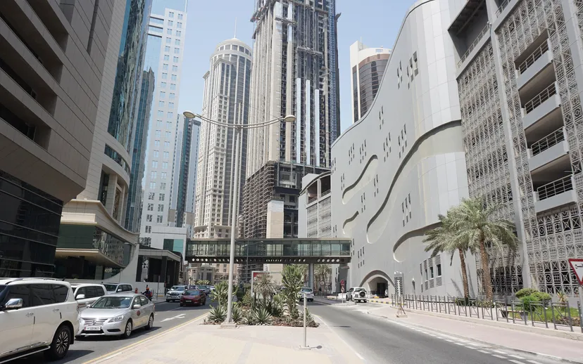 A street in Doha's Al Dafna business district is lined with office towers, palms and parked cars.