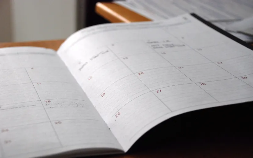 An open monthly planner lying on a desk, with dates in a grid and a few handwritten notes.