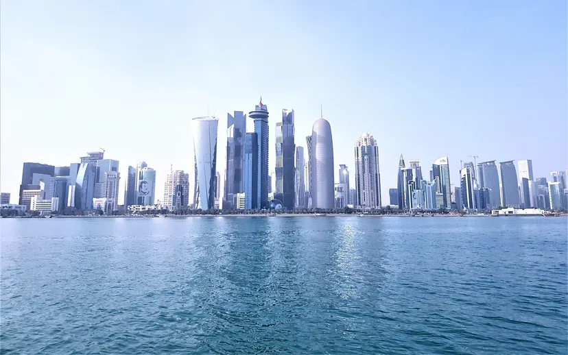 The West Bay skyline of Doha seen across calm blue water on a clear day.