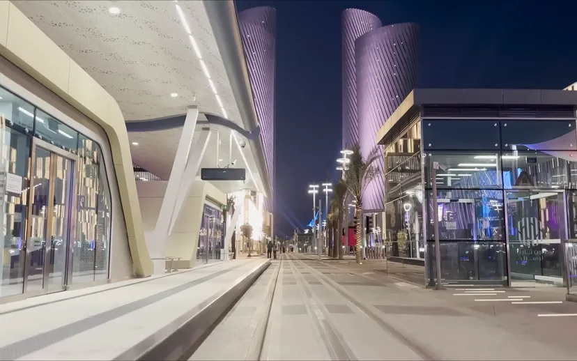 Lusail Boulevard at dusk, with glass shopfronts and the lit Lusail Plaza office towers ahead.