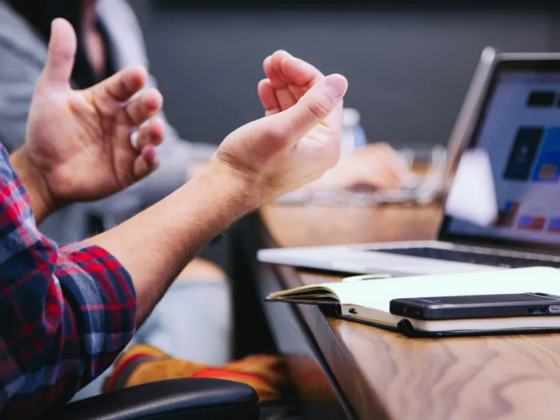 Hands gesturing during a meeting beside a laptop and a notebook