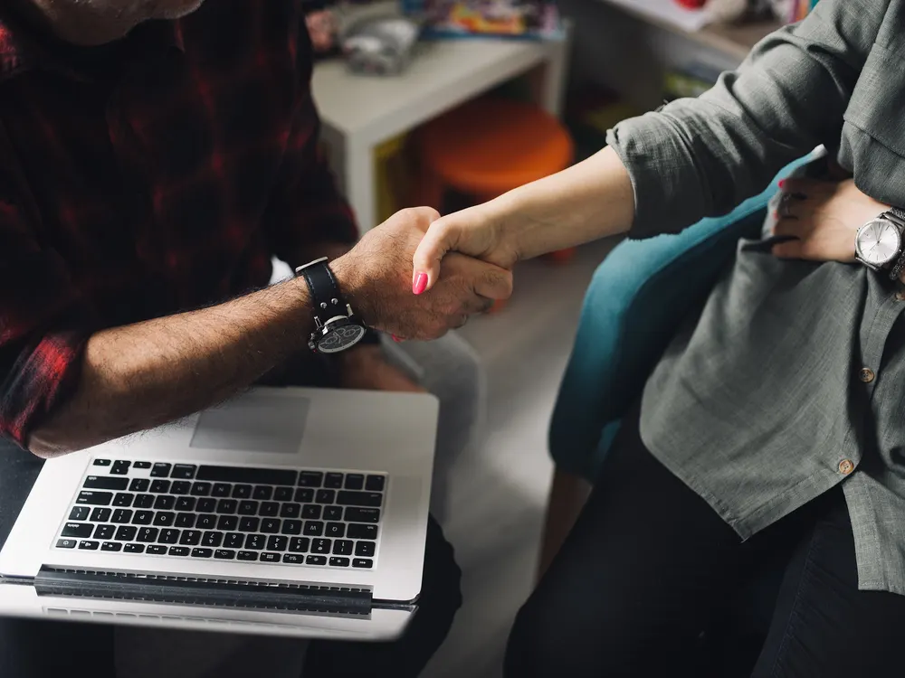 Two people shaking hands over a laptop