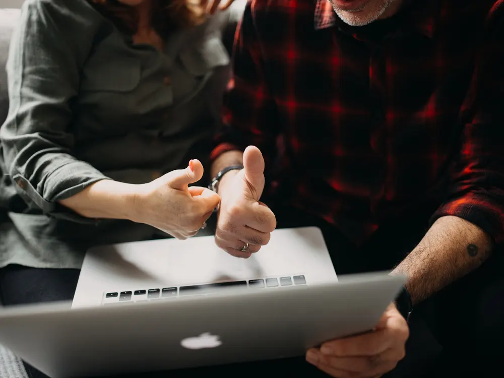 Two people looking at a laptop together, one giving a thumbs up