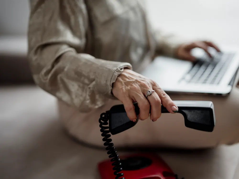 A person holding a telephone receiver while working on a laptop