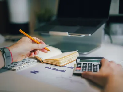 A person working with a calculator and a notebook beside printed figures